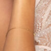 Femme en robe dentelle blanche portant un bracelet Mya en or fin, chaîne, fleur, fond blanc Laparitaine
