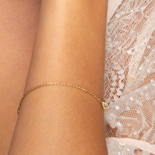 Femme en robe dentelle blanche portant un bracelet Mya en or fin, chaîne, fleur, fond blanc Laparitaine